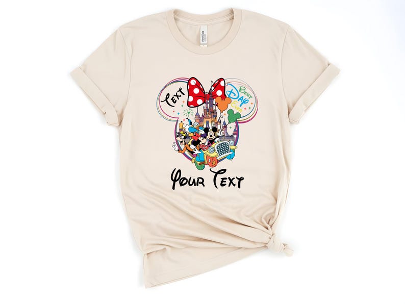 May include: Cream-colored t-shirt featuring a colorful Disney graphic. The design includes Mickey and Minnie Mouse, a castle, and the text "Best Day Ever" and "Your Text". A red polka-dot bow is at the top of the design.