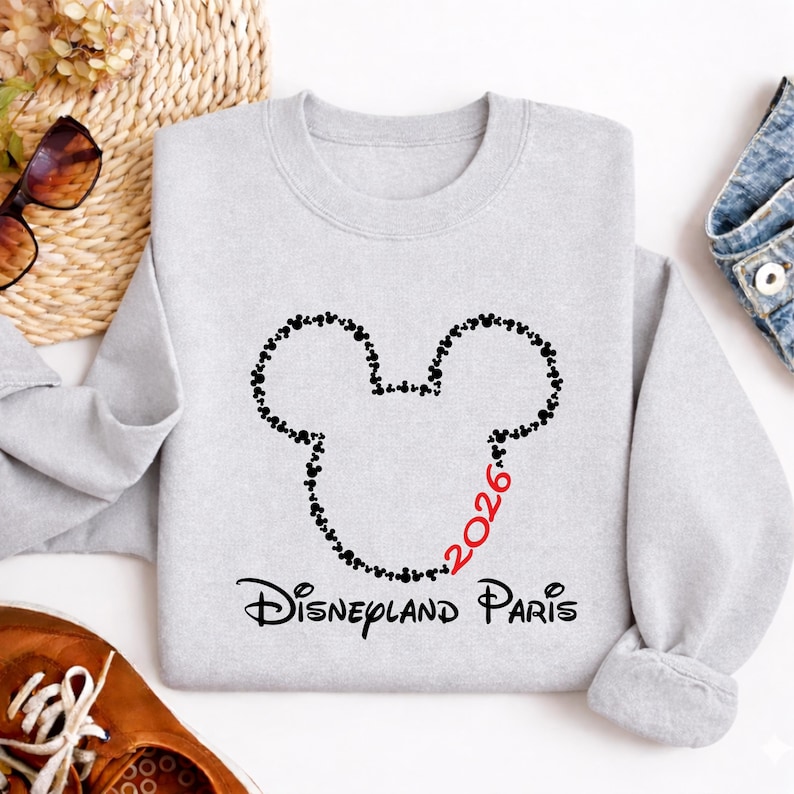 May include: A light gray sweatshirt featuring a Mickey Mouse head outline made of small black hearts. The number "2026" is in red, and the words "Disneyland Paris" are printed in black below the design. The sweatshirt is made of a soft material.