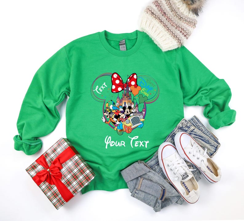 May include: Green sweatshirt featuring a Minnie Mouse bow and a Disney character design. The design includes the text "Text" and "Your Text". A gift box with a red bow and a winter hat are also in the image.