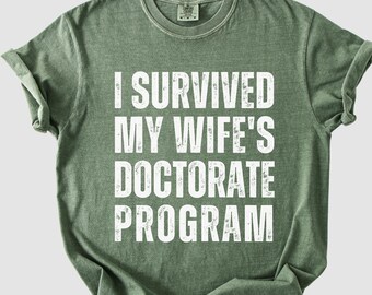 Camiseta Comfort Colors "Sobreviví al programa de doctorado de mi esposa", regalo para esposo, camiseta divertida de graduación de doctorado, camiseta de disertación de doctorado, camiseta de broma de graduación