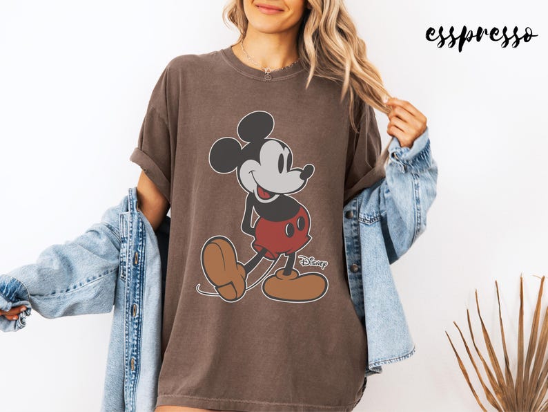 May include: Brown t-shirt featuring a classic Mickey Mouse graphic. The cartoon character is depicted in black, white, red, and brown. The word "Disney" is printed below the character. The word "esspresso" is printed in the upper right corner.