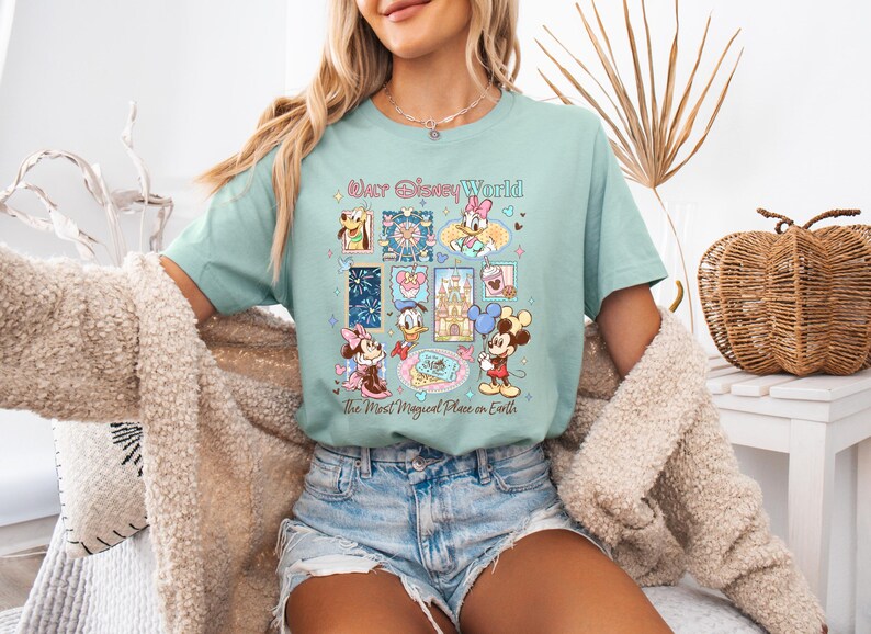 K&ouml;nnte beinhalten: Hellblaues T-Shirt mit einer farbenfrohen Grafik mit Disney-Figuren und dem Text "Our Disney World, the Most Magical Place on Earth". Das Design enth&auml;lt Bilder von Mickey Mouse, Minnie Mouse und anderen Figuren.