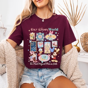 K&ouml;nnte beinhalten: Burgunderfarbenes T-Shirt mit einer farbenfrohen Grafik von Disney-Figuren und -Attraktionen, darunter Micky Maus, Donald Duck und Aschenputtels Schloss. Der Text "Walt Disney World" und "The Most Magical Place on Earth" sind ebenfalls abgebildet.