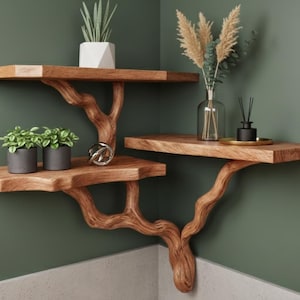 Op de afbeelding: Houten hoekplanken met een uniek takontwerp. De planken bevatten potplanten, decoratieve items en een vaas met droogbloemen. De planken zijn gemaakt van natuurlijk hout en zijn bevestigd aan een groene muur.