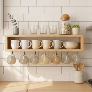 Könnte beinhalten: Ein Küchenregal aus Holz zeigt weiße und beige Tassen, Schalen und Gläser. Ein Glas mit Holzdeckel ist mit Bohnen gefüllt. Eine kleine Topfpflanze und eine Vase mit einem Zweig befinden sich ebenfalls auf dem Regal. Tassen hängen an Haken.