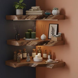 May include: Three wooden shelves in a corner, displaying home decor items. The top shelf holds a potted plant, folded towels, and a decorative glass bowl. The middle shelf features candles, incense, and a framed print. The bottom shelf has bottles, candles, and a small Buddha statue.
