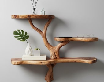 Pode incluir: Uma prateleira de parede de madeira em forma de árvore, com três níveis. O grão natural da madeira é visível, e a prateleira é adornada com objetos decorativos, incluindo um vaso branco, uma planta verde, livros e uma pequena suculenta.