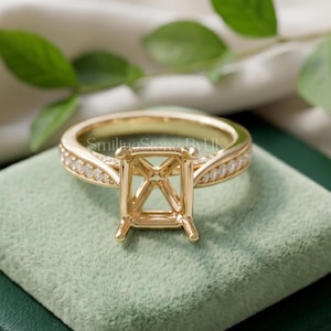May include: A gold ring setting featuring an empty rectangular prong mount designed for a center stone. The band is accented with a row of small pavé-set diamonds along each side. The metal has a polished finish and the text SmilingStoneByUK is visible.