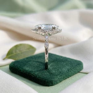 Angled sparkle of a personalized 925 sterling silver custom engagement ring. Brilliant D color VVS1 clarity moissanite catches the light beautifully. Intricate navette shape band enhances this affordable luxury bespoke jewelry. Excellent floral setting gem, nature inspired gem, moissanite bridal set, minimalist dainty detail, vintage bridal set, and sustainable lab gem alternative.
