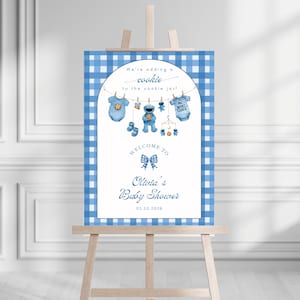Könnte beinhalten: Babyparty-Schild mit blau-weißem Vichy-Karo-Rand. Die Illustration zeigt Babykleidung, ein Cookie Monster und den Text "We're adding a cookie to the cookie jar!" und "Welcome to Olivia's Baby Shower".