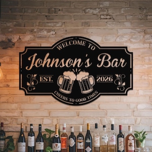 Könnte beinhalten: Schwarzes Metallschild mit dem Text "Welcome to Johnson's Bar" und "Cheers to Good Times". Es zeigt zwei Bierkrüge, die anstoßen. Das Schild enthält auch das Jahr "2026" und das Wort "Est."