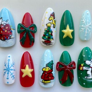 May include: A set of ten almond-shaped, painted fingernails with Christmas-themed designs. The nails feature images of Snoopy, Christmas trees, bows, and snowflakes in various colors, including red, green, blue, and white.
