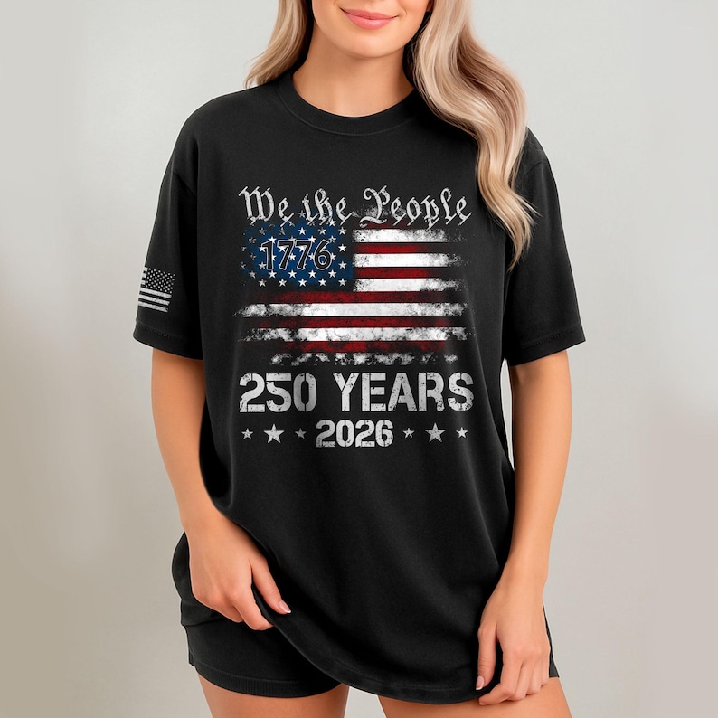 May include: Black t-shirt featuring a distressed American flag design with the text "We the People 1776" above the flag and "250 YEARS 2026" below. The shirt has a classic crew neck and short sleeves.