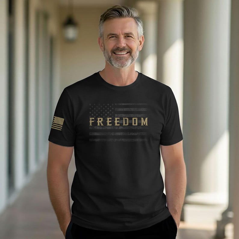 May include: Black t-shirt featuring a distressed American flag design with the word "FREEDOM" in a gold color. The shirt has a crew neck and short sleeves. A small American flag is on the left sleeve.