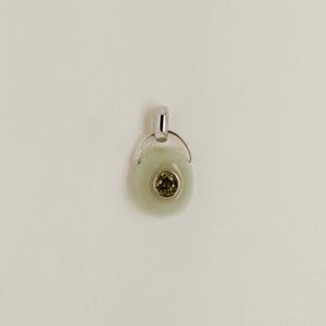 Puede incluir: Un colgante verde claro con una fianza plateada. El colgante tiene forma ovalada con una piedra circular verde oliva en el centro. La fianza es de dise&ntilde;o simple y curvado, sobre un fondo neutro.