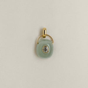 Puede incluir: Colgante de oro con una piedra ovalada de color verde claro y una peque&ntilde;a piedra redonda y transparente en el centro. El colgante tiene una argolla dorada y un anillo dorado que conecta la argolla con la piedra.