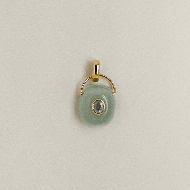Puede incluir: Colgante de oro con una piedra ovalada de color verde claro y una peque&ntilde;a piedra redonda y transparente en el centro. El colgante tiene una argolla dorada y un anillo dorado que conecta la argolla con la piedra.