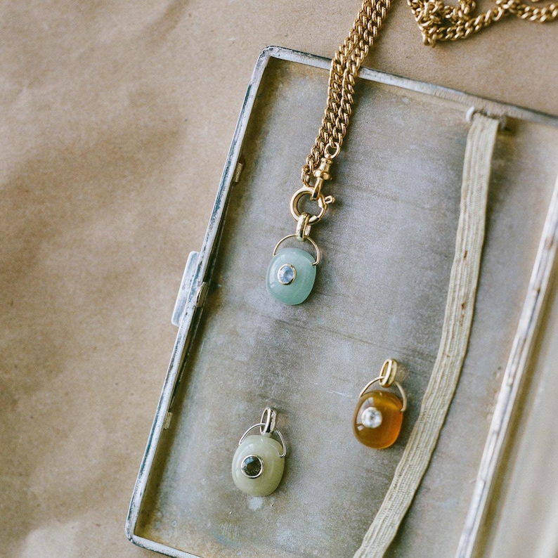 Puede incluir: Tres collares con colgantes de piedras preciosas en un estuche de metal de estilo vintage. Los colgantes tienen detalles met&aacute;licos dorados y peque&ntilde;as piedras preciosas redondas. Las piedras son de color verde, amarillo y transparente.