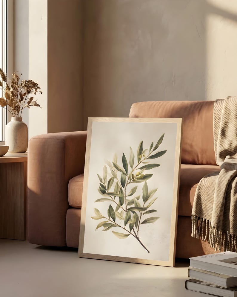 May include: A framed botanical print featuring a detailed illustration of an olive branch with green leaves and small yellow olives. The artwork is set against a soft, off-white background and framed in light wood.