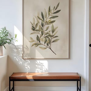 May include: A framed botanical print featuring a detailed illustration of olive branches with green leaves and small yellow fruits. The artwork is displayed above a brown leather bench with a black metal frame, creating a stylish interior design.