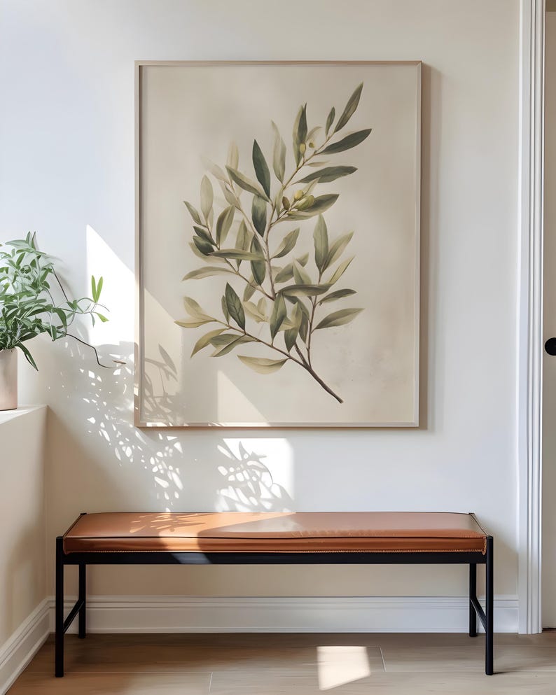 May include: A framed botanical print featuring a detailed illustration of olive branches with green leaves and small yellow fruits. The artwork is displayed above a brown leather bench with a black metal frame, creating a stylish interior design.