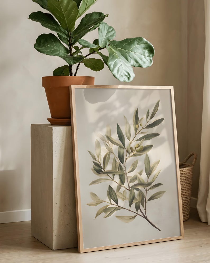 May include: A framed botanical print featuring a detailed illustration of olive branches with green and yellow-green leaves. The print has a light beige background and a natural wood frame. A potted plant sits on a concrete pedestal.