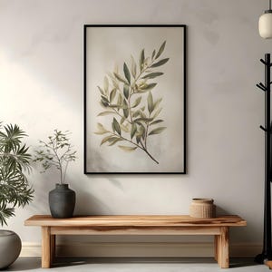 May include: A framed botanical print featuring a watercolor illustration of olive branches with green and yellow leaves. The artwork hangs above a wooden bench, with a dark vase and a woven basket adding to the decor. The room has a neutral color palette.