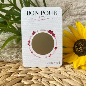 May include: A white gift card with the words "BON POUR" and a heart symbol at the top. A gold scratch-off circle is in the centre, surrounded by a red heart-decorated circle. The words "Gratte vite!" are at the bottom.