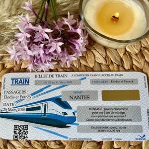 Peut inclure: Un billet de train bleu et blanc avec une illustration de train. Le billet est daté du 25 mars 2026 et comprend les noms Elodie et Franck. Une bougie allumée et des fleurs violettes sont en arrière-plan.
