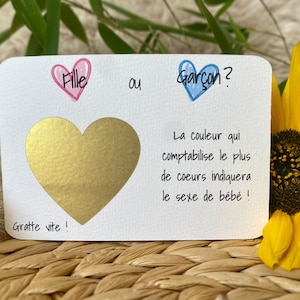 Peut inclure: Une carte blanche avec un cœur doré à gratter, des illustrations de cœurs roses et bleus, et du texte en français. Le texte comprend "Fille ou Garçon ?" et des instructions pour révéler le sexe du bébé. Une tournesol est en arrière-plan.
