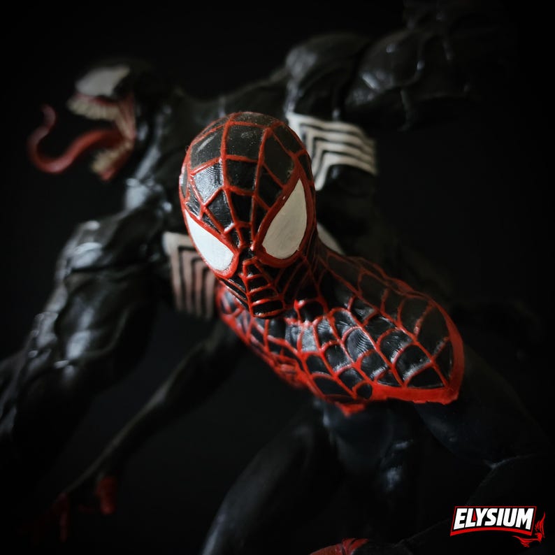 Puede incluir: Una figura de acci&oacute;n de Spider-Man negra y roja con lentes blancos, posando frente a una figura de Venom negra. La figura de Spider-Man tiene un dise&ntilde;o de patr&oacute;n de telara&ntilde;a roja. El fondo es oscuro.