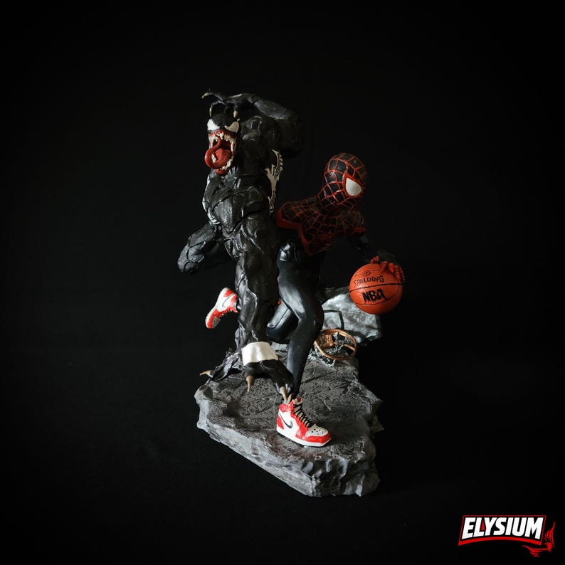 Puede incluir: Figura detallada que representa a Venom y Spider-Man jugando al baloncesto. Venom es negro con una lengua roja, mientras que Spider-Man lleva un traje rojo y negro. El bal&oacute;n de baloncesto es naranja con "NBA" impreso. La base es gris y los zapatos son rojos y blancos.