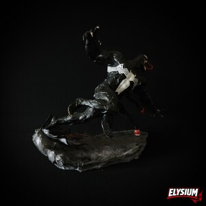 Puede incluir: Una escultura din&aacute;mica de Venom, un personaje de Marvel Comics, en una pose de lucha. La figura es predominantemente negra con marcas blancas en forma de ara&ntilde;a y una lengua roja. Est&aacute; montada sobre una base gris texturizada sobre un fondo negro. La palabra "ELYSIUM" est&aacute; en la esquina inferior derecha.
