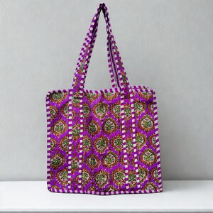 May include: A purple tote bag featuring a repeating floral design in green, red, and white. The bag has a striped border and handles in a matching purple and white checkered pattern. The bag is on a white surface.