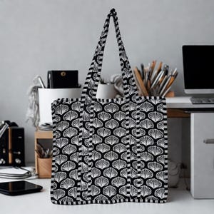 May include: A black and white tote bag featuring a seashell pattern. The bag has two handles and a rectangular shape. The seashell design is repeated across the entire surface of the bag.