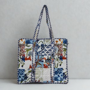 May include: A patterned tote bag with a patchwork design. The bag features floral and abstract patterns in blue, white, red, and green. The handles and edges are trimmed with a blue and white striped fabric. The bag is suitable for carrying items.