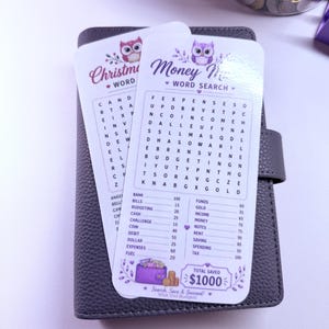 May include: Two white rectangular laminated cards featuring a purple owl graphic and a word search puzzle titled Money Maze. The cards list financial terms like Bank, Bills, and Budgeting with corresponding values, ending with a Total Saved $1000 box.