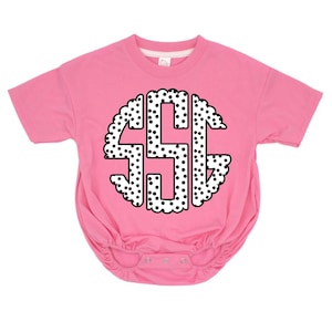 May include: A pink baby bodysuit with a white and black polka dot monogram design. The monogram features the letters "SSG" in a circular pattern with a scalloped edge. The bodysuit has short sleeves and snap closures.