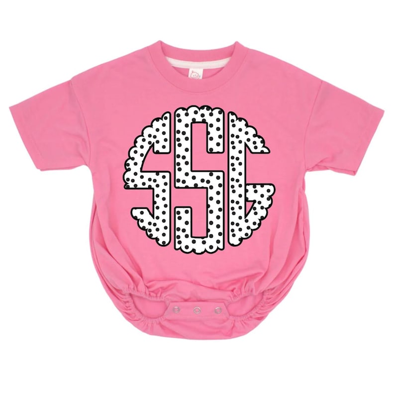 May include: A pink baby bodysuit with a white and black polka dot monogram design. The monogram features the letters "SSG" in a circular pattern with a scalloped edge. The bodysuit has short sleeves and snap closures.