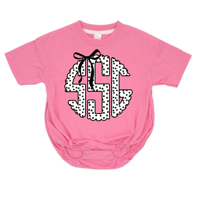 May include: Pink baby bodysuit with a white and black polka dot monogram design. The monogram is in a scalloped circle shape and features a black bow at the top. The bodysuit has short sleeves and snap closures.