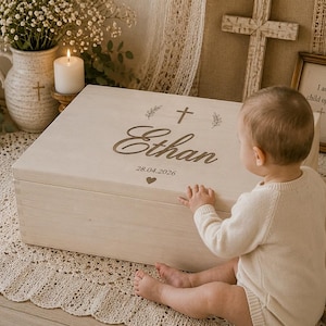 May include: A rectangular light-colored wooden keepsake box featuring a hinged lid engraved with the name Ethan, a cross symbol, two sprigs, the date 28.04.2026, and a small heart icon. The box has a smooth, light-toned finish and clean edges.