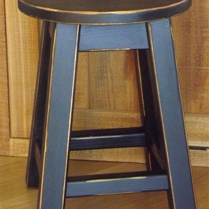 May include: A black wooden stool with a distressed finish and a round seat. The stool has a simple design with three legs and a single crossbar.