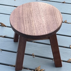 May include: A round wooden stool with a dark brown finish and three legs. The stool is made of solid wood and has a smooth, polished surface.