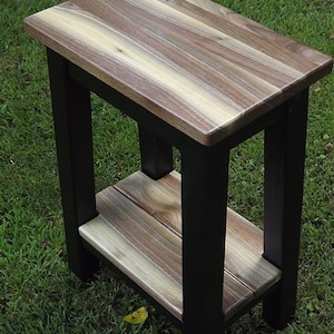 May include: A small wooden end table with a black painted frame and a natural wood top and shelf. The wood has a unique grain pattern with shades of brown, gray, and white.
