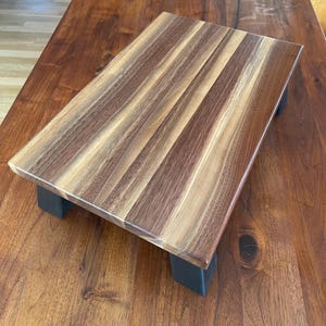 May include: A rectangular wooden serving tray with a natural walnut finish and black metal legs. The tray has a smooth surface and a rich wood grain pattern.