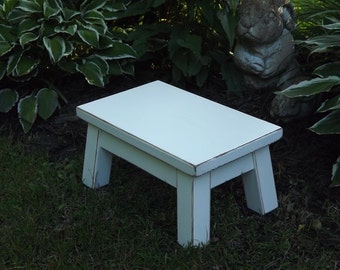 May include: White wooden step stool with a distressed finish. The stool has a square top and four legs.