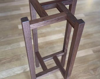 May include: A wooden plant stand with a square base and four legs. The stand is made of dark brown wood and has a simple, geometric design.
