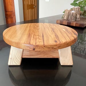 May include: A round wooden table with a natural wood finish and a unique, asymmetrical base. The table has a light brown color and is made of solid wood.