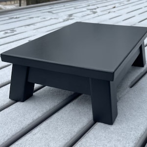 May include: A black wooden step stool with a smooth, flat top surface and four sturdy legs.