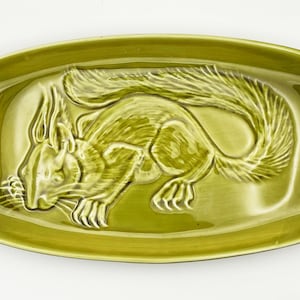 Op de afbeelding: Een groene keramische serveerschaal met een reliëf ontwerp van een eekhoorn. De rechthoekige schaal heeft afgeronde hoeken en een glanzende afwerking. De eekhoorn is afgebeeld in een gedetailleerde, naturalistische stijl.